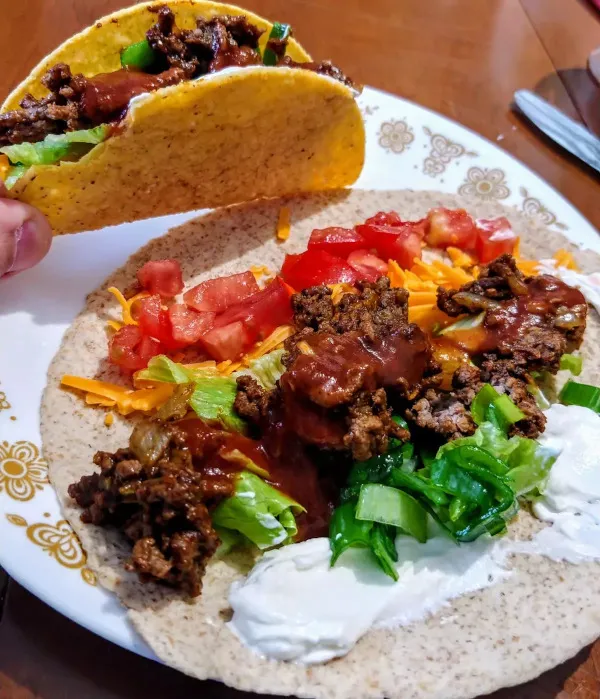 A hard-shell beef taco held over a soft tortilla topped with beef, tomato, cheese, lettuce, green onion and sour cream